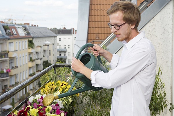 Човек полива цветя на балкона